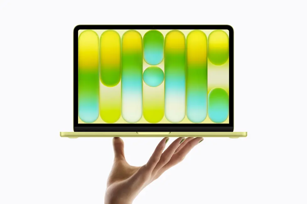 MacBook Neo held in one hand — Citrus color with green wallpaper
